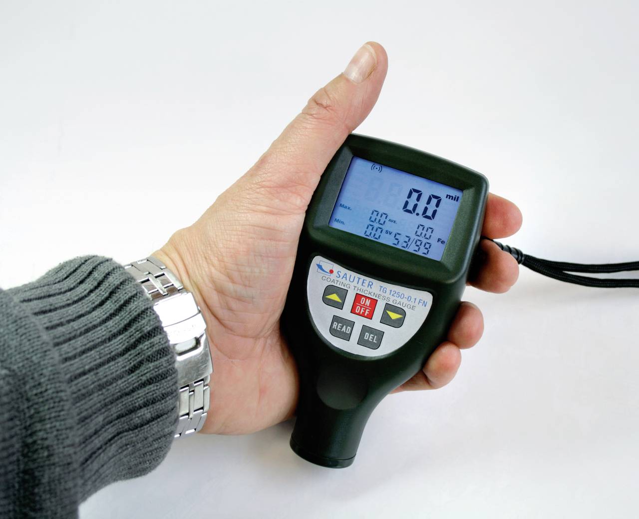 Eine Hand hält ein Gerät zur Messung von Oberflächenspannungen. Der Bildschirm zeigt '0.0' an. Gerät hat Tasten 'READ' und 'DEL'.