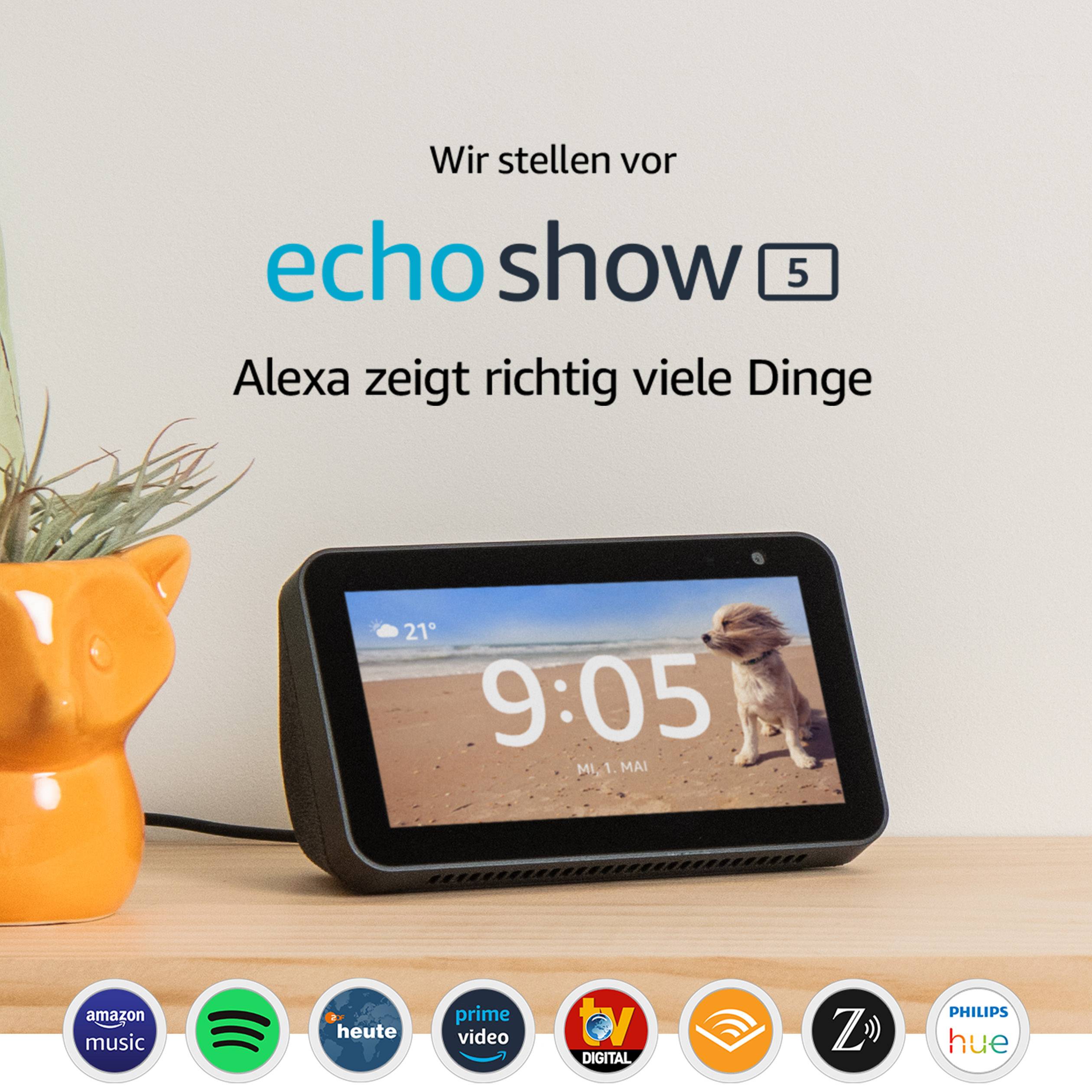 Ein Echo Show 5 auf einem Tisch mit einer Pflanzenvase daneben. Der Bildschirm zeigt die Uhrzeit 9:15, darunter Text 'Alexa zeigt viele Dinge'.