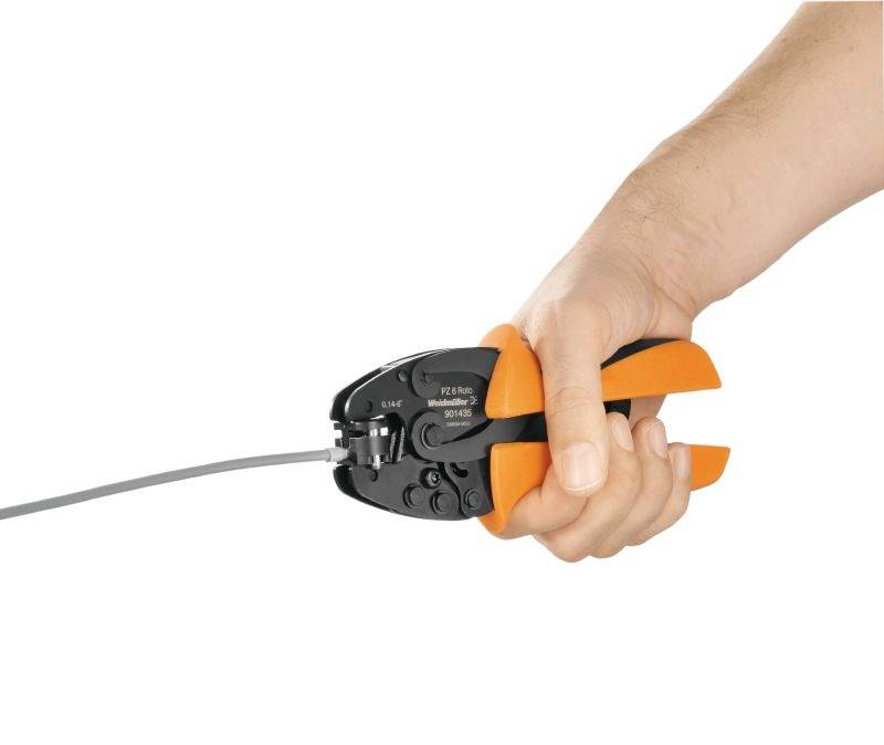 Eine Hand hält eine orange-schwarze Crimpzange, die ein Kabel bearbeitet.