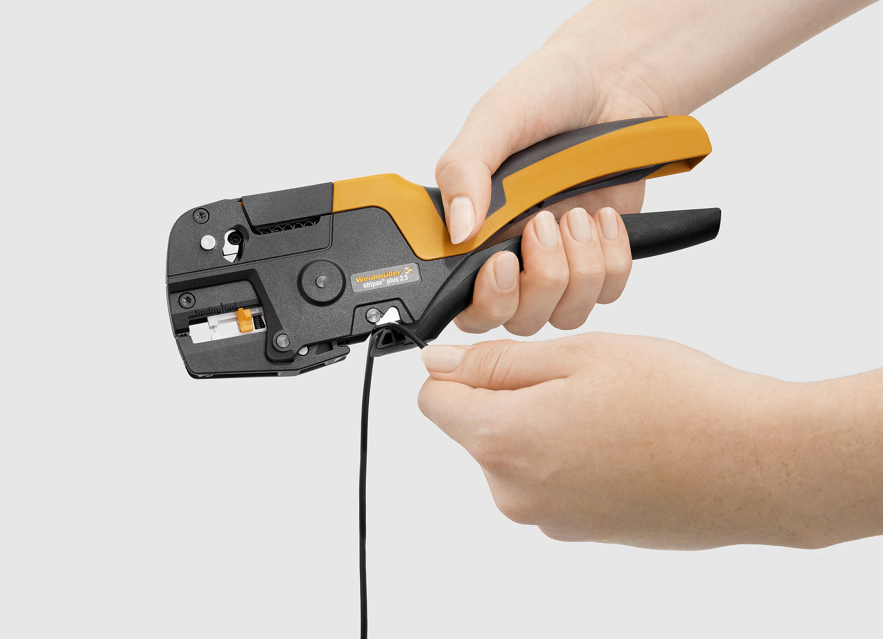 Eine Person verwendet ein orange-schwarzes Crimpwerkzeug, um ein Kabel zu crimpen. Hände und Werkzeug sind deutlich sichtbar.