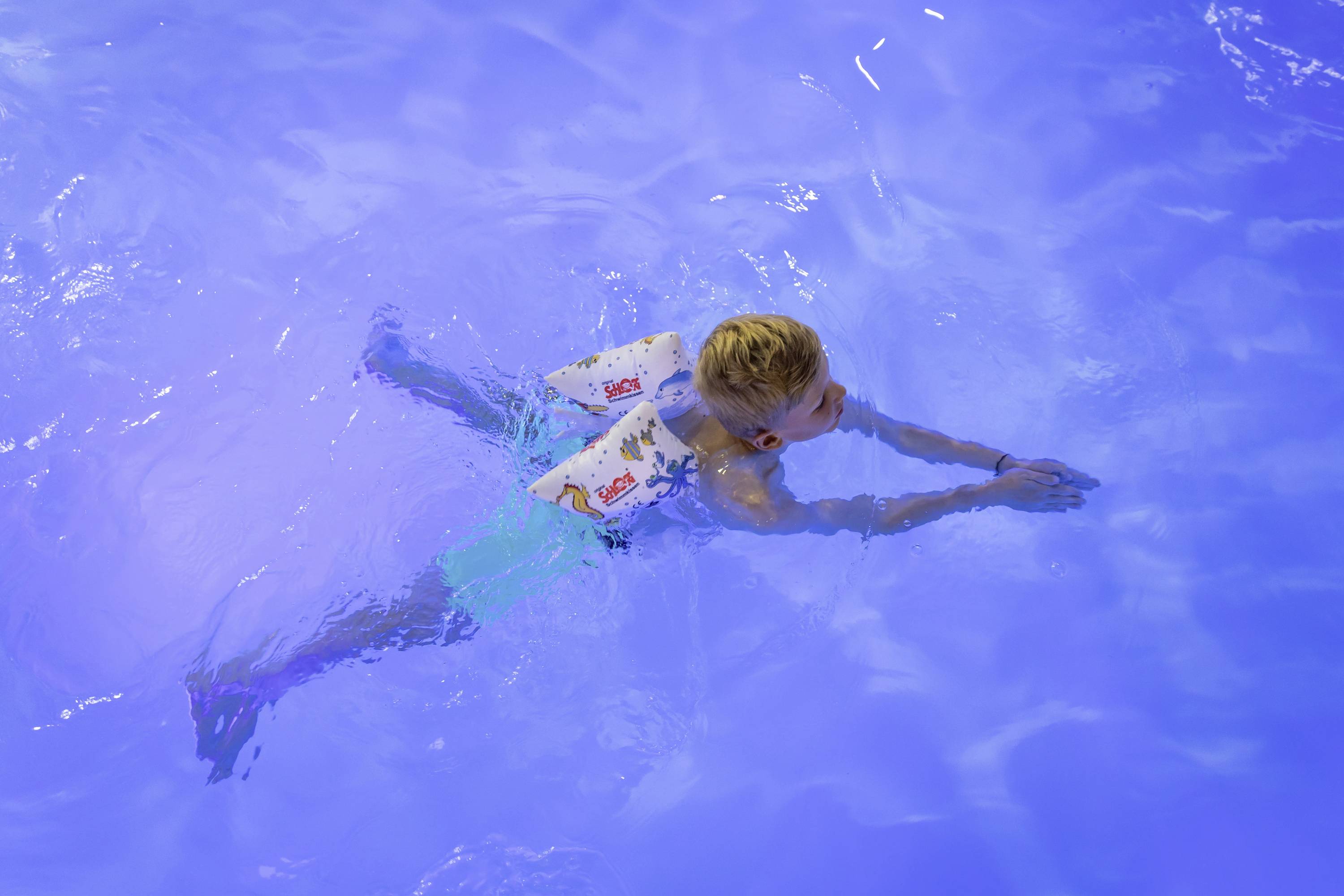 Ein Kind mit Schwimmflügeln schwimmt in einem blauen Pool.