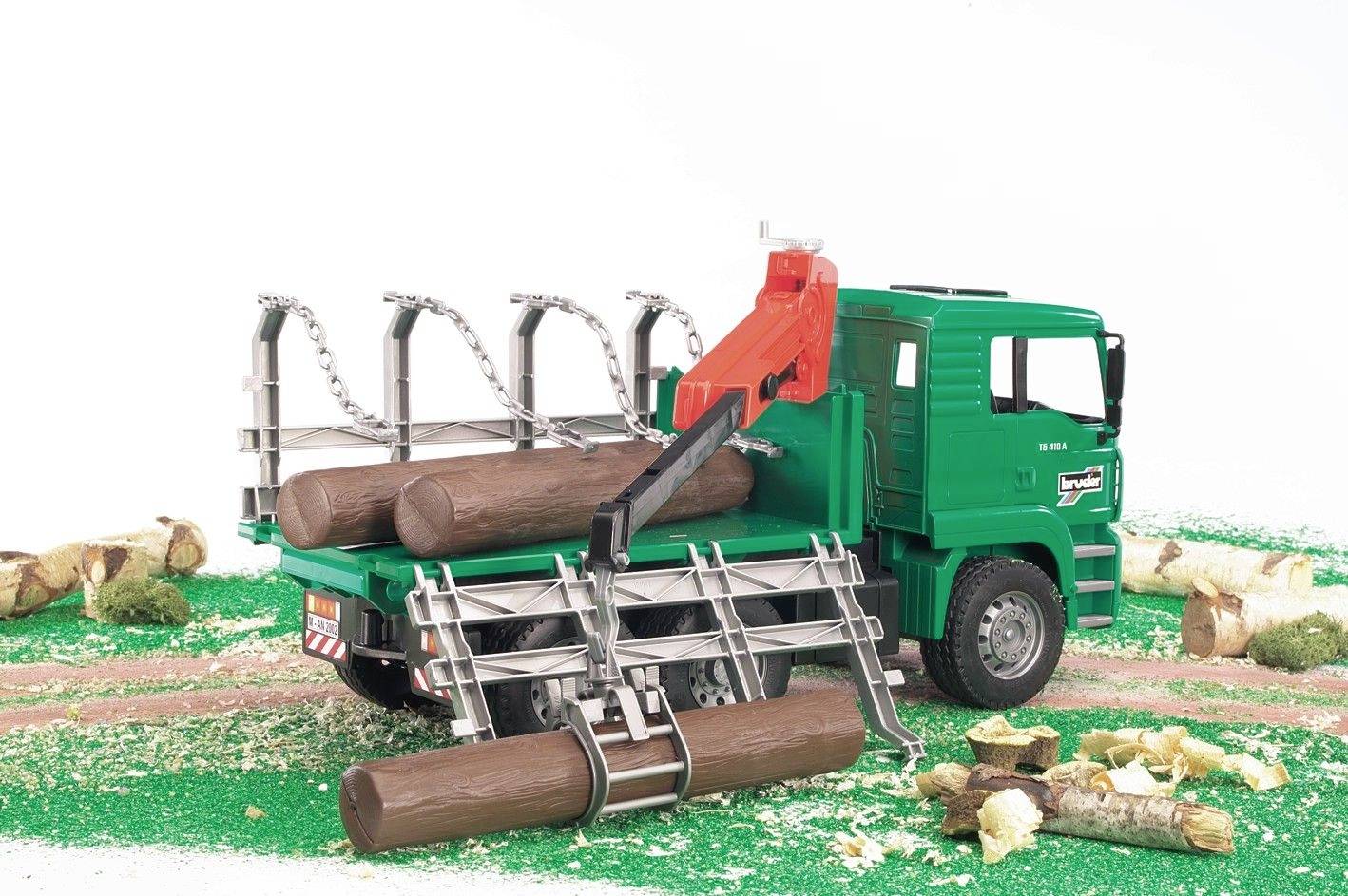 Ein grüner Spielzeug-LKW mit Holzkran lädt Baumstämme auf seiner Ladefläche, umgeben von Holzstücken auf grünem Untergrund.
