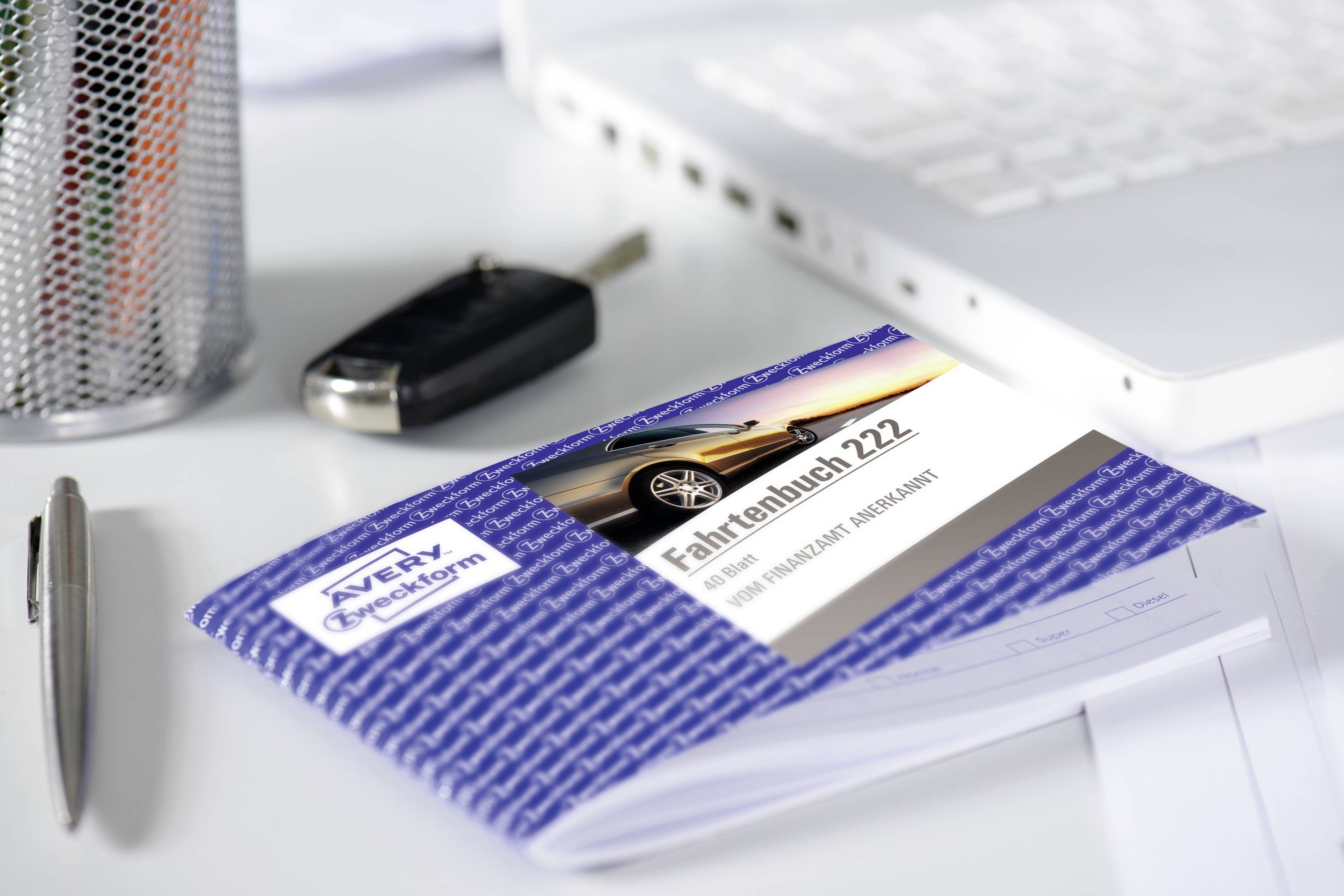 Ein blaues Fahrtenbuch mit Autosymbol liegt auf einem Schreibtisch neben einem Stift, Autoschlüssel und Laptop.