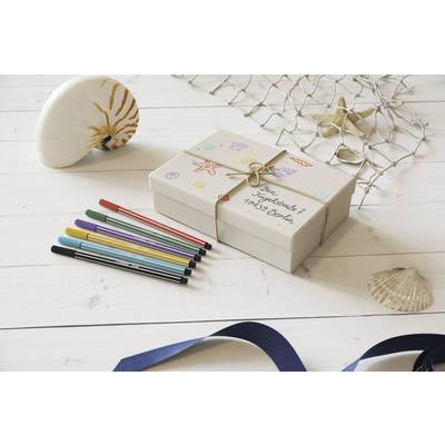 Eine dekorierte Geschenkbox mit der Aufschrift 'Zum Geburtstag!'. Daneben liegen bunte Stifte. Im Hintergrund sind Muscheln zu sehen.