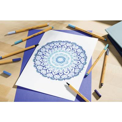 Ein detailliertes Mandala in Blau- und Türkistönen auf weißem Papier, umgeben von farbigen Stiften auf einem Tisch.