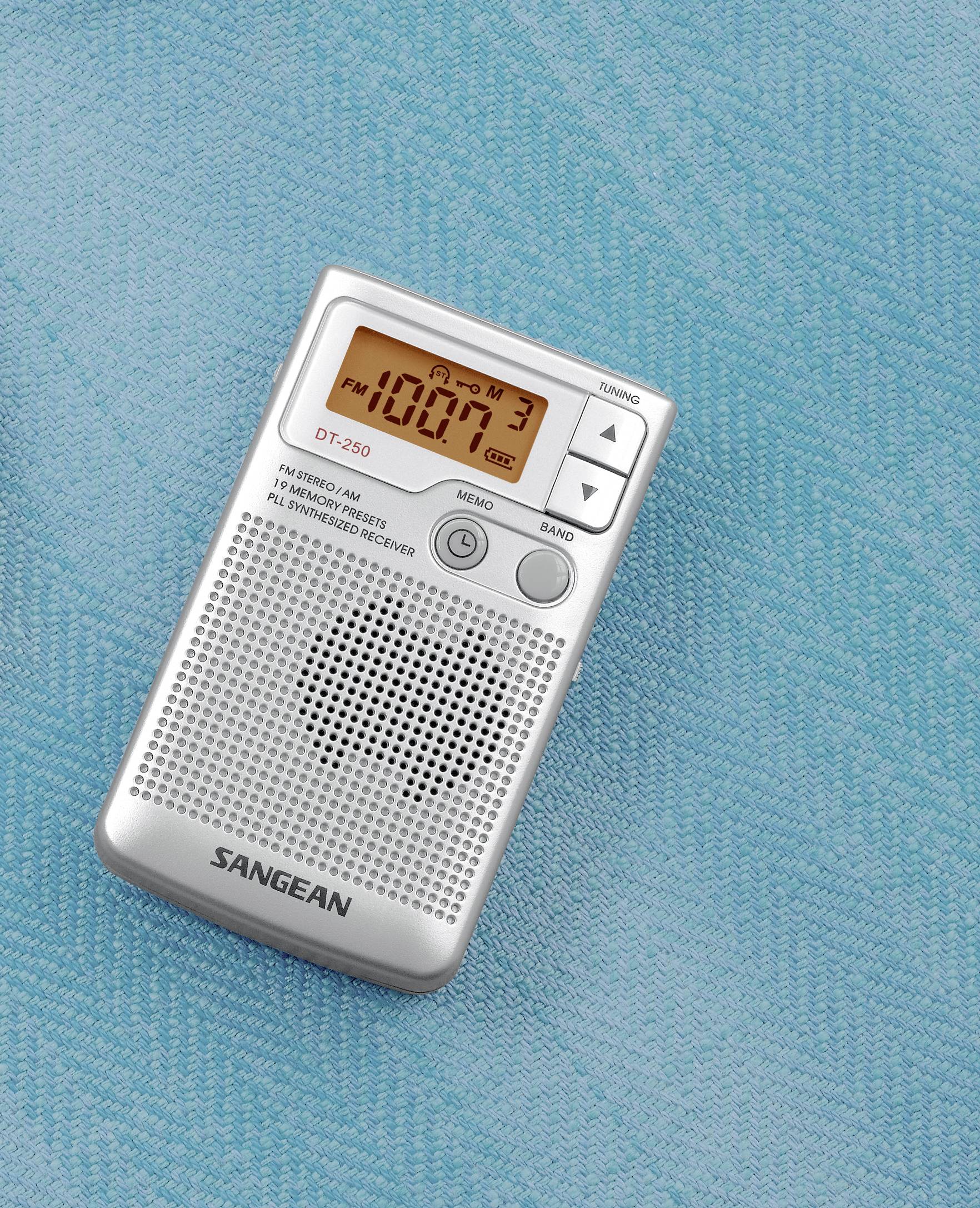 Ein tragbares Radio zeigt eine FM-Frequenz von 108.7 MHz auf einem digitalen Display an. Liegt auf einem türkisfarbenen Stoff.