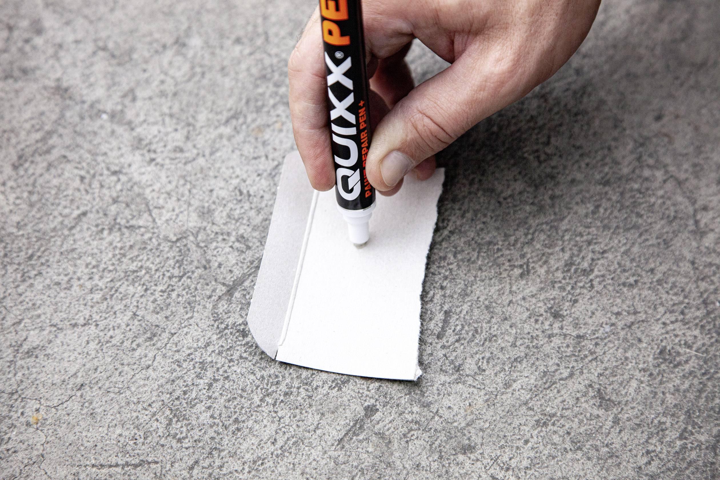Hand hält einen Stift, schreibt auf ein kleines Stück Papier, das auf einer Betonoberfläche liegt.