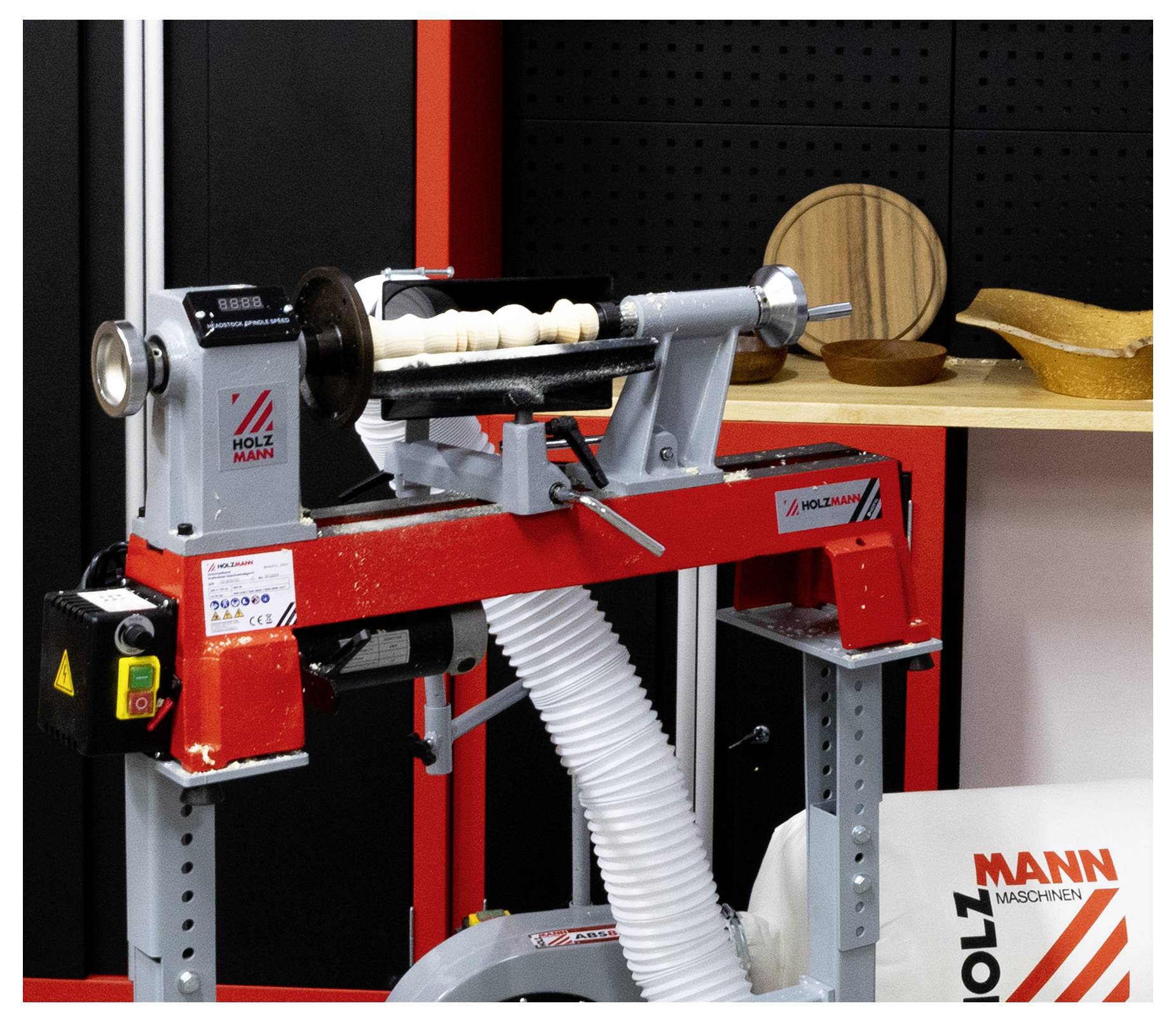 Drehmaschine für Holzbearbeitung mit einem aufgespannten Holzrohling und Absaugschlauch in einer Werkstatt-Ausstellung.