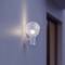 Eine moderne Wandleuchte mit runder Glaskugel leuchtet gegen eine blaue Wand und beleuchtet einen angrenzenden Raum leicht.