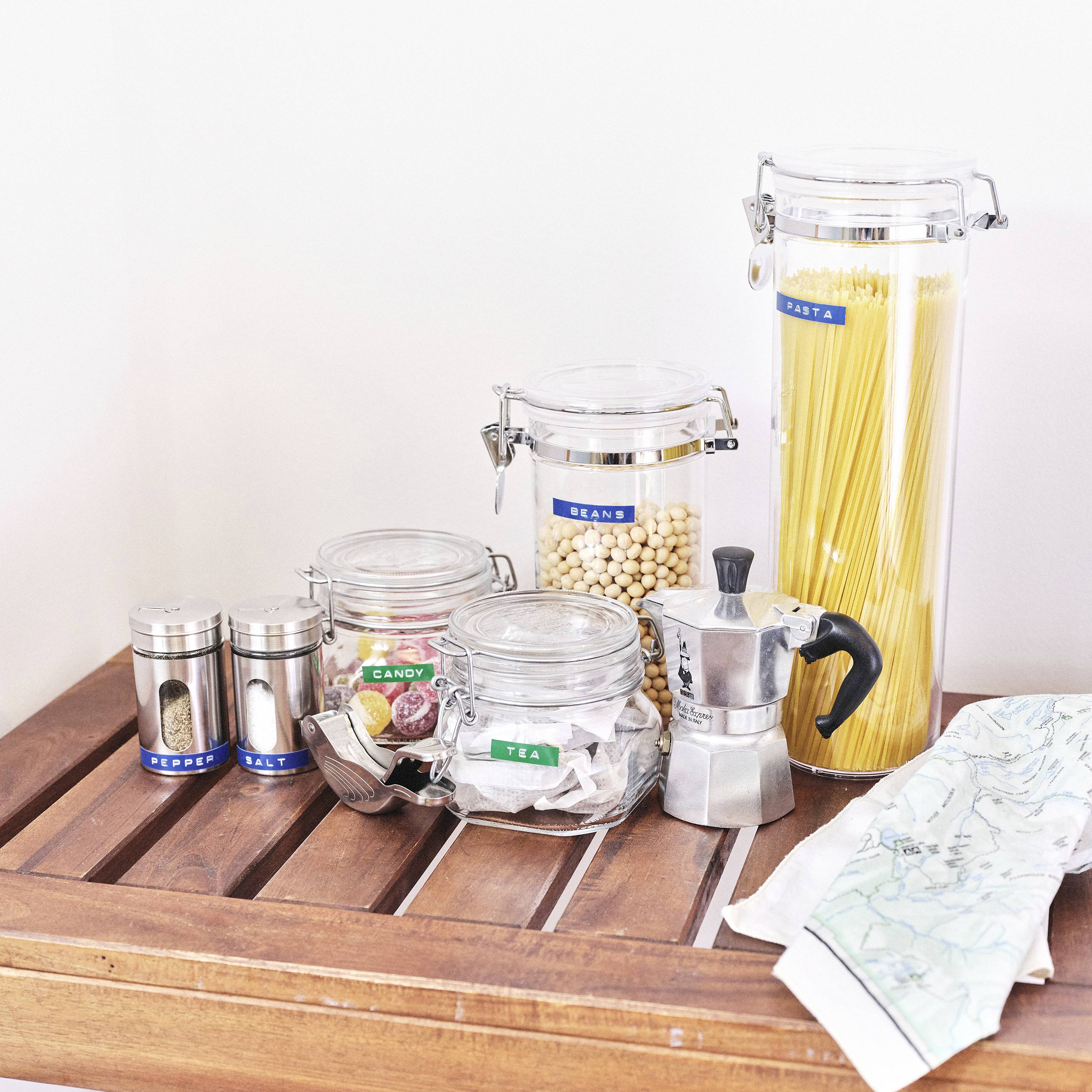 Verschiedene Vorratsgläser auf einem Tisch: Pasta, Kekse und Bonbons. Daneben eine kleine Espressokanne und Servietten.