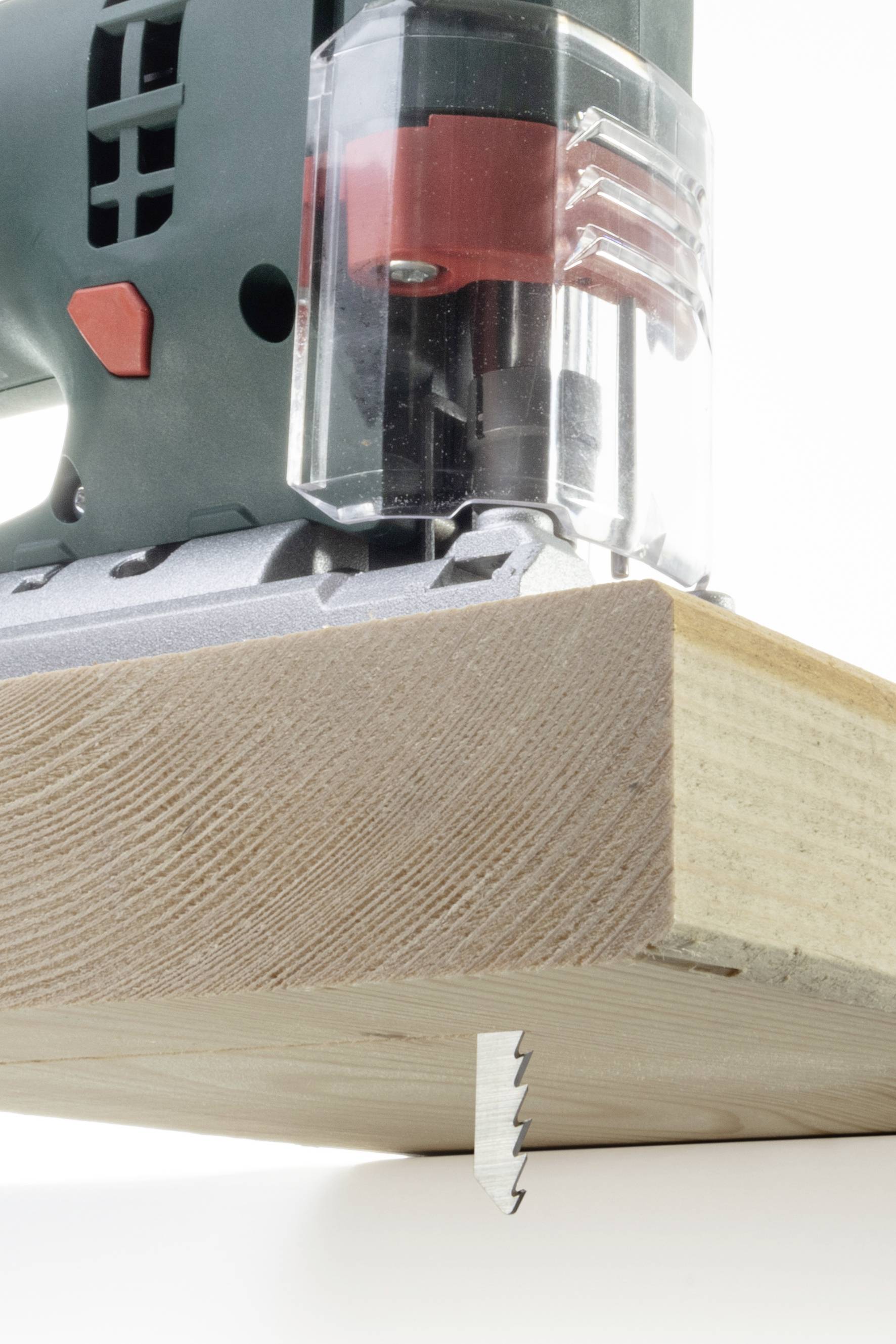 Eine Stichsäge schneidet durch ein Holzbrett. Die Maschine ist grün mit roten Elementen. Fokus liegt auf dem Sägeblatt im Einsatz.