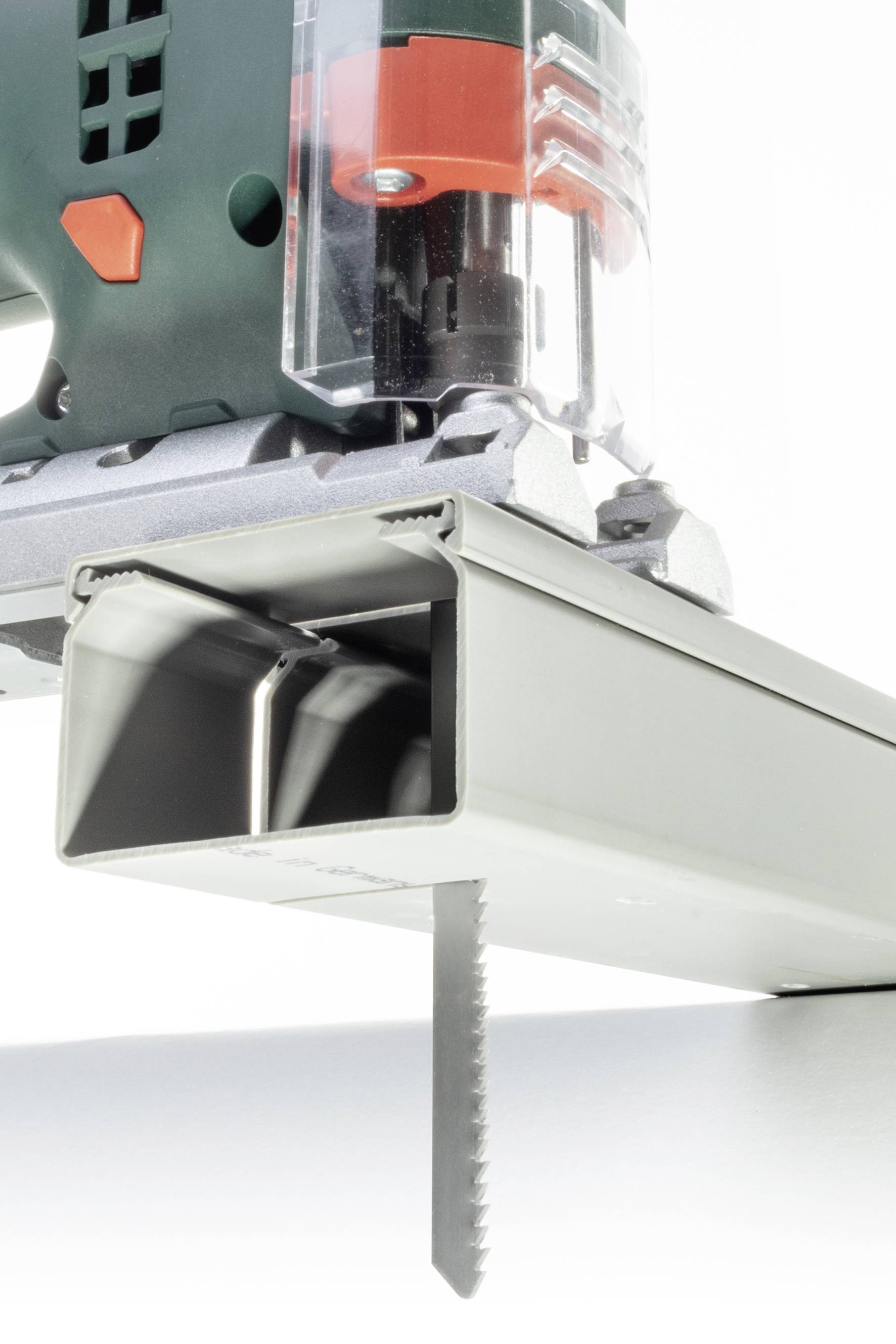 Eine elektrische Stichsäge schneidet präzise durch ein Metallrohr. Die Säge besitzt ein grünes Gehäuse und ein scharfes Sägeblatt.