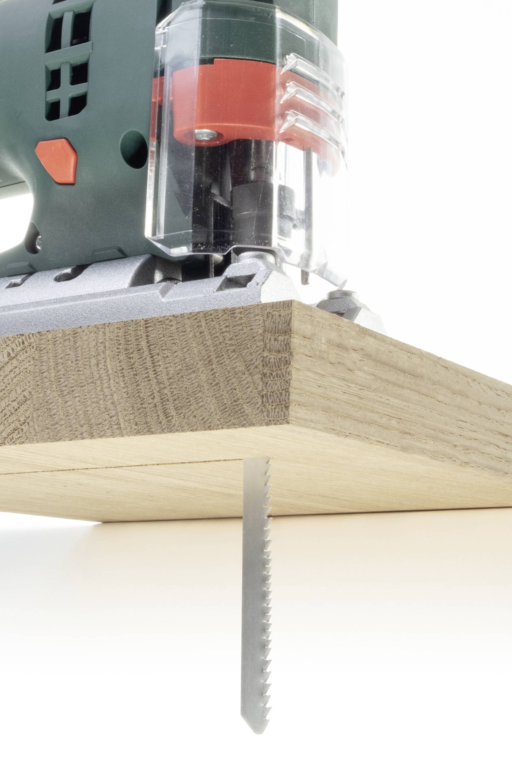 Eine Stichsäge schneidet an der Kante eines Holzbret ts, Spiralzahn-Sägeblatt sichtbar unter dem Brett.