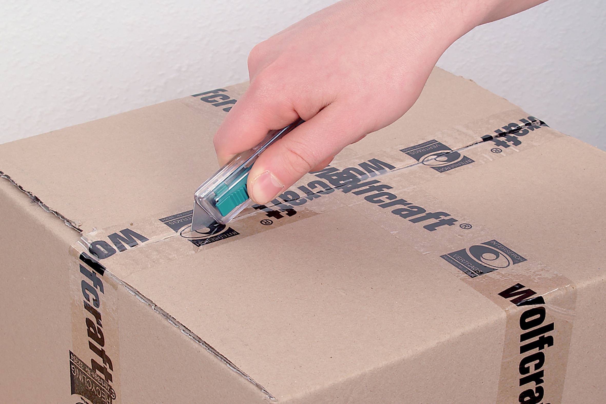 Eine Hand schneidet mit einem Cutter-Messer Klebeband auf einem Karton durch.