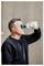 Ein Mann in einem schwarzen Hemd benutzt eine tragbare Augenspülflasche, um sein Auge zu spülen, während er vor einem neutralen Hintergrund steht.