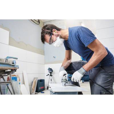 Ein Mann mit Schutzbrille und Maske schneidet Fliesen mit einer elektrischen Schneidemaschine in einem unfertigen Raum.