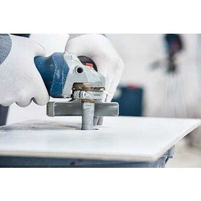 Eine Person schleift die Kante einer weißen Platte mit einer elektrischen Schleifmaschine. Hände tragen weiße Handschuhe.