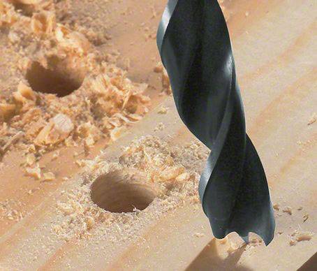 Eine Bohrmaschine bohrt ein Loch in ein Holzbrett. Sägespäne sind um die gebohrten Löcher verstreut.