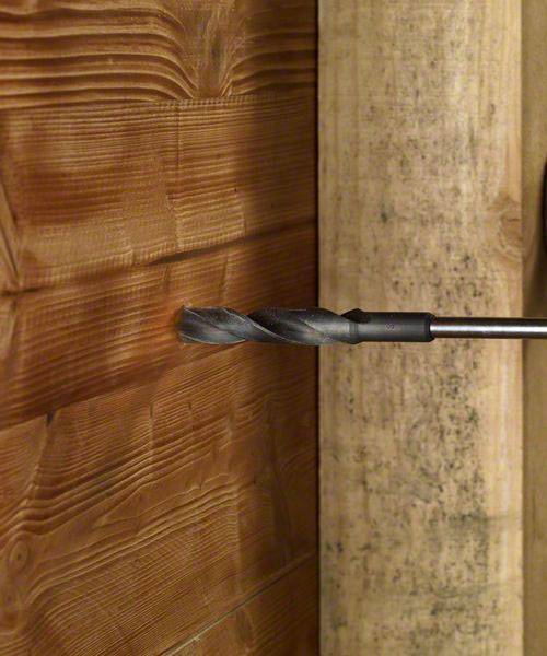 Ein Bohrer, der in eine Holzplatte gebohrt wird. Die Oberfläche zeigt deutliche Holzmaserung und der Bohrer ist gerade in Aktion.