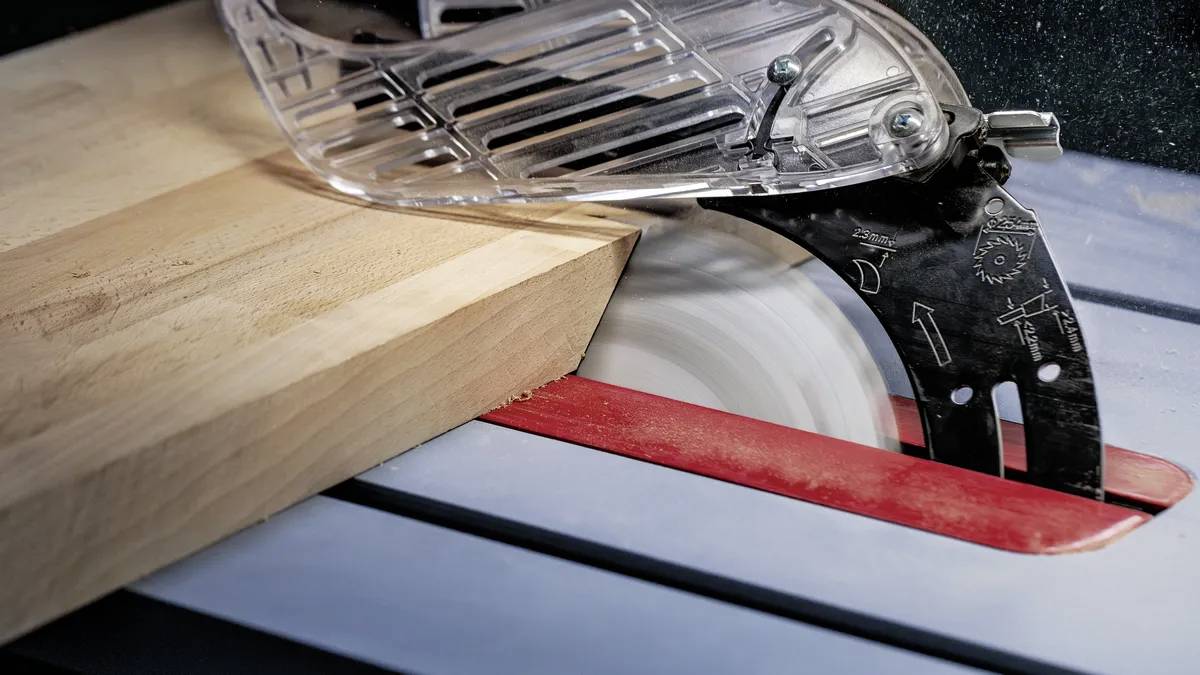 Eine Kreissäge schneidet eine Holzplanke. Die Sägeblatt dreht sich, und ein Sicherheitsschutz bedeckt das Blatt teilweise.