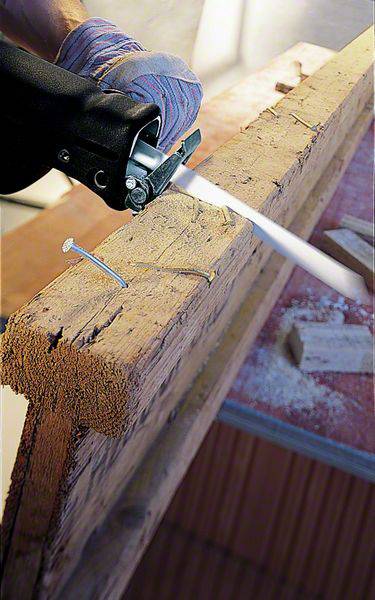 Eine elektrische Säbelsäge schneidet einen großen Holzbalken. Ein Handschuh hält die Säge, während Staub in der Luft schwebt.
