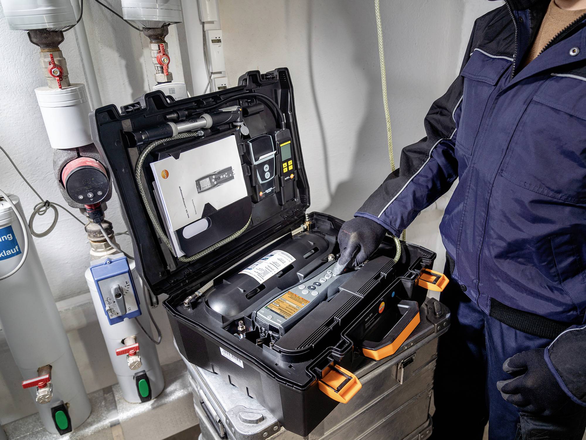 Eine Person in Arbeitskleidung überprüft eine geöffnete technische Ausrüstung in einem industriellen Raum.