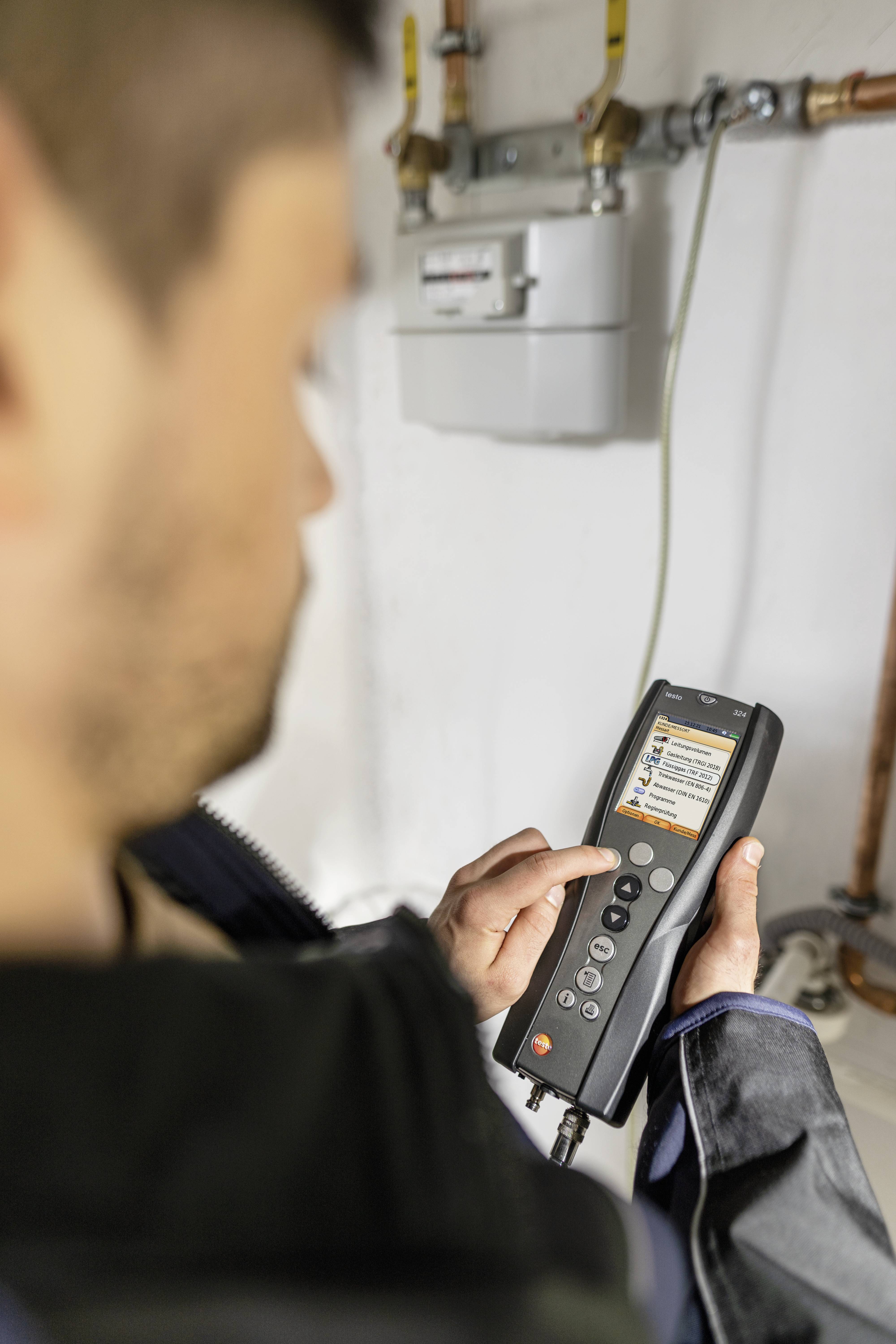 Eine Person verwendet ein Handgerät zur Messung von Gasleitungen in einem Technikraum.