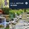 'Aqua Active 12.000' Teichfilter System. Bild zeigt Wasserfall mit üppigem Grün und Steinen, umgeben von Gartenlandschaft.