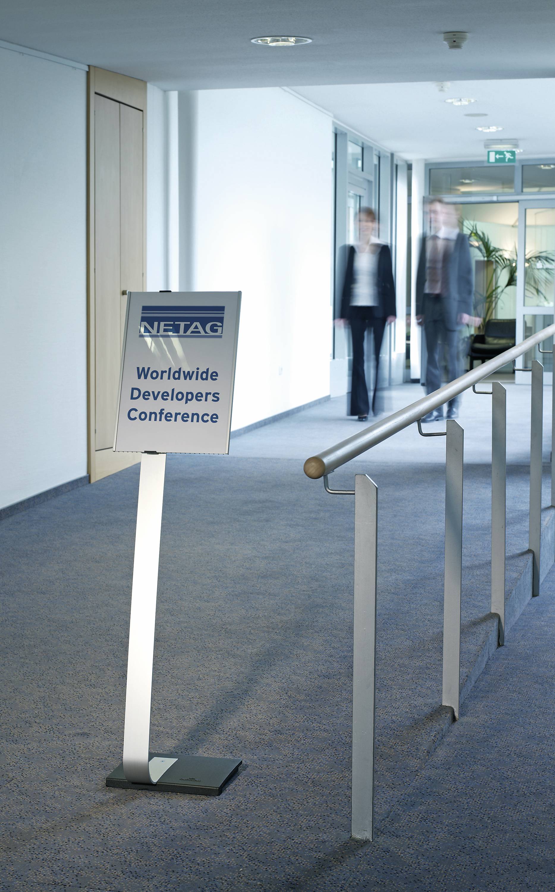 Zwei Personen gehen in einem Flur. Ein Schild zeigt 'Worldwide Developers Conference' an.
