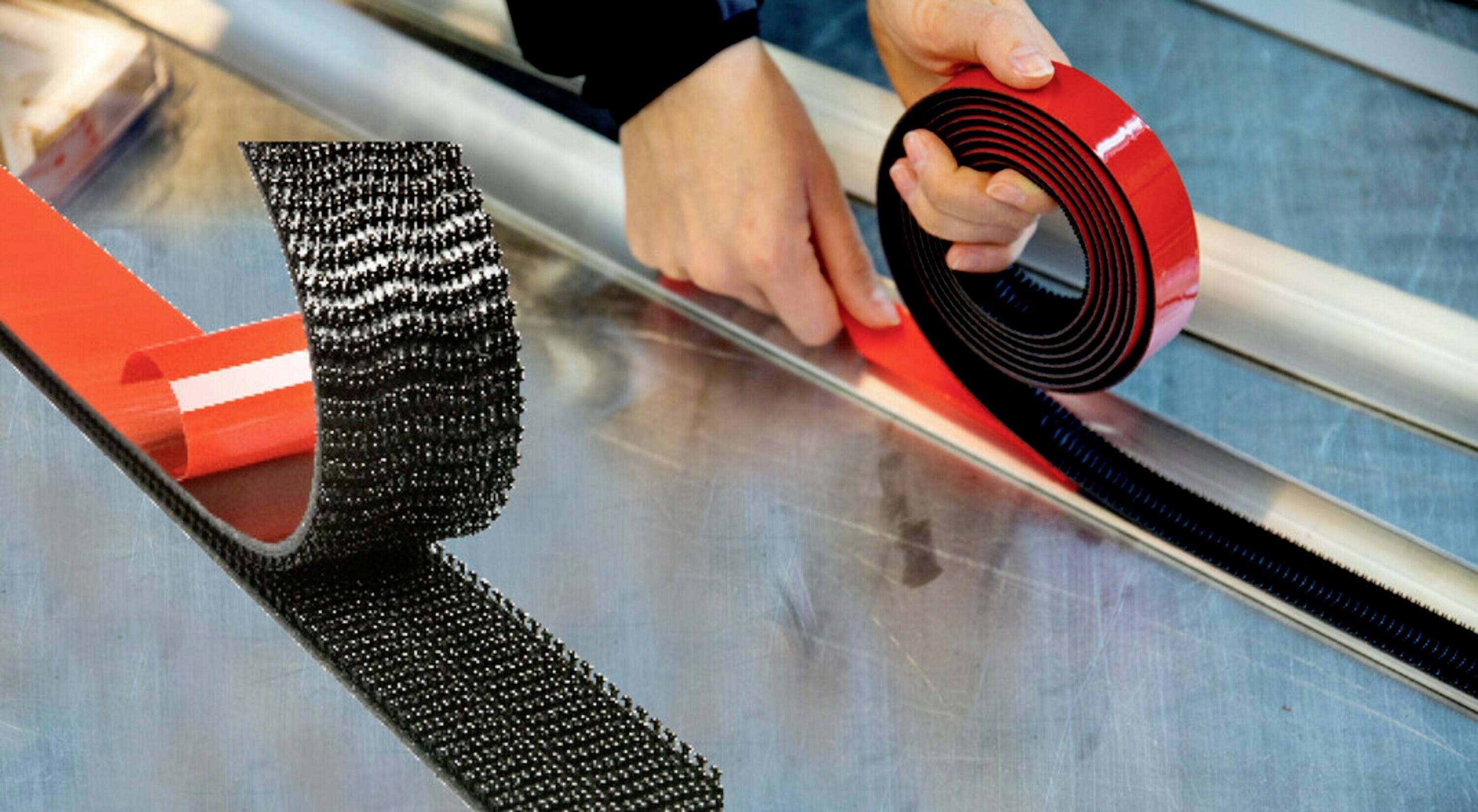 Person, die Klettband auf eine Metalloberfläche aufbringt. Hände halten das Band und drücken es fest.