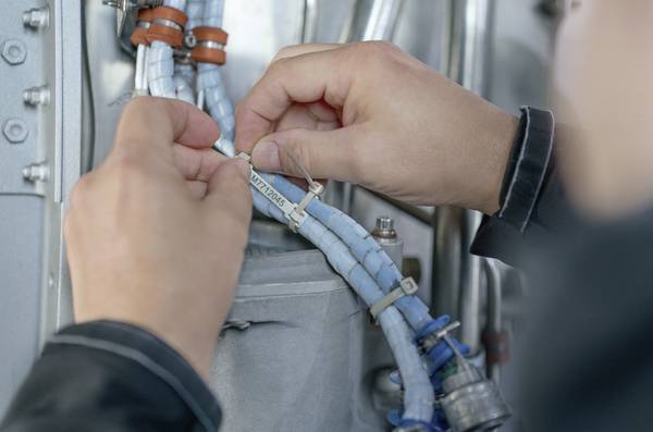 Eine Person prüft Kabel in einer technischen Umgebung, hält diese mit einer Hand und befestigt sie mit einer Kabelbinderzange.