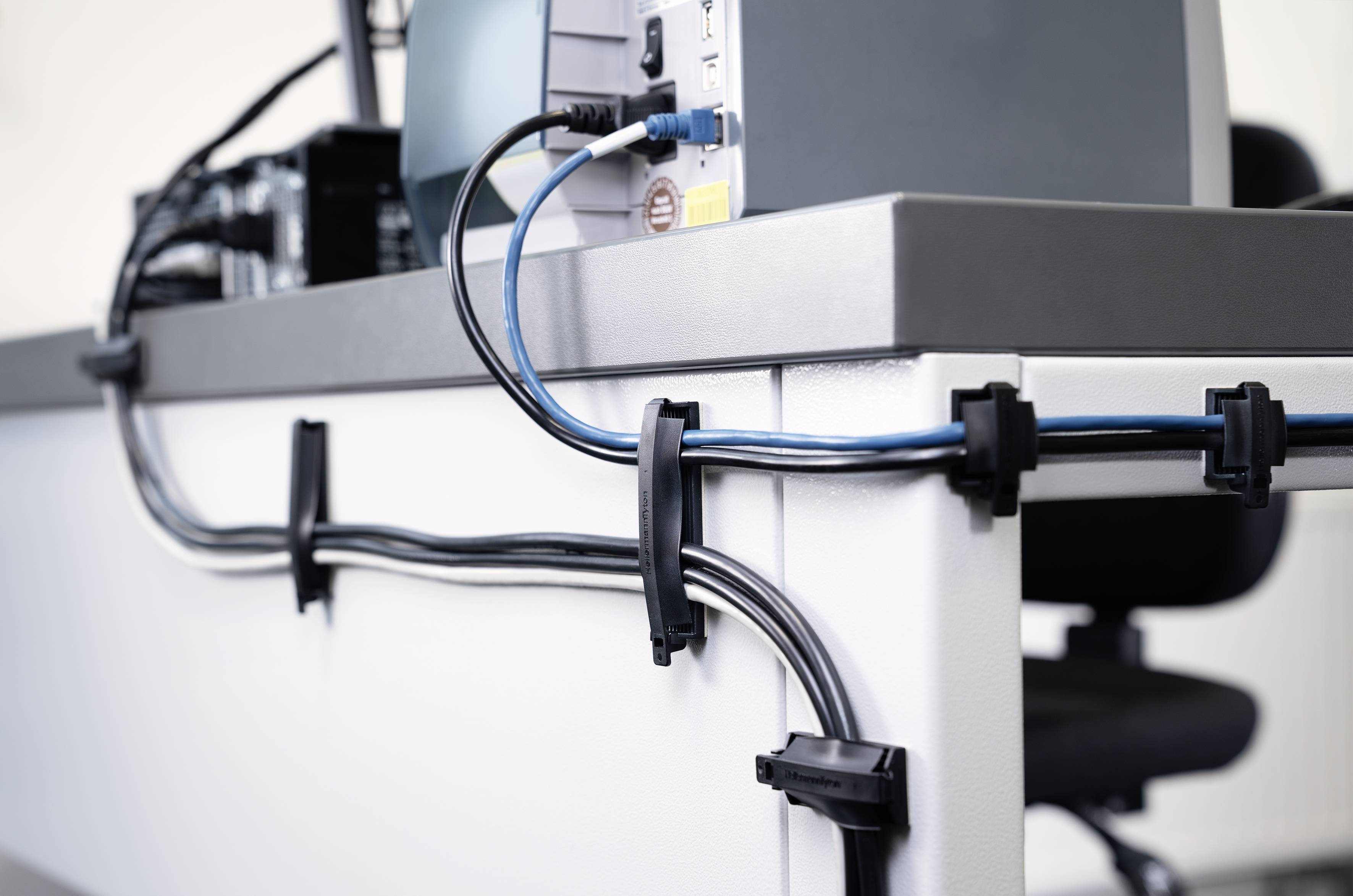 Kabel sind ordentlich an einem Schreibtisch befestigt. Der Fokus liegt auf der Kabelorganisation mit Clips und Führung.