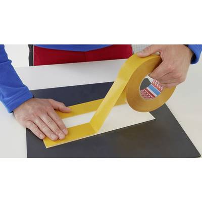 Eine Person klebt gelbes Klebeband auf ein rechteckiges Stück Papier auf einem Tisch. Hände sind sichtbar, während das Band abgewickelt wird.