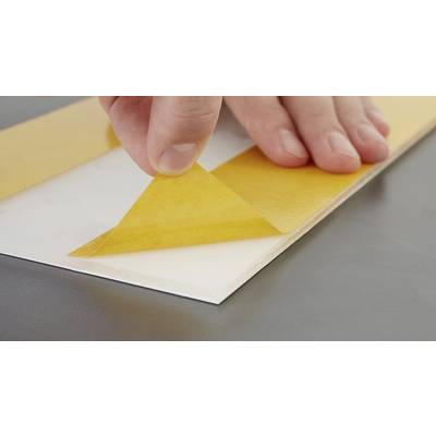 Hand entfernt gelbes Schutzpapier von klebender Fläche auf grauem Tisch.