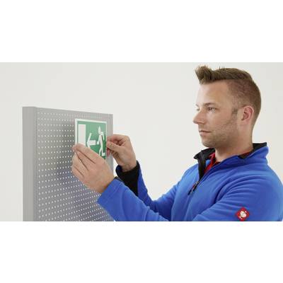 Ein Mann in blauer Jacke befestigt ein grünes Notausgangsschild an einer perforierten Tafel.