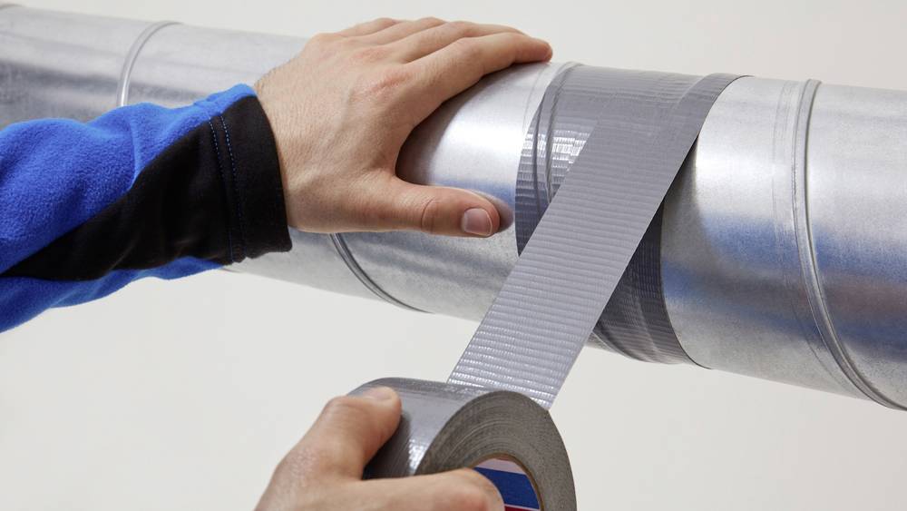 Eine Person klebt ein silbernes Klebeband auf ein Metallrohr.