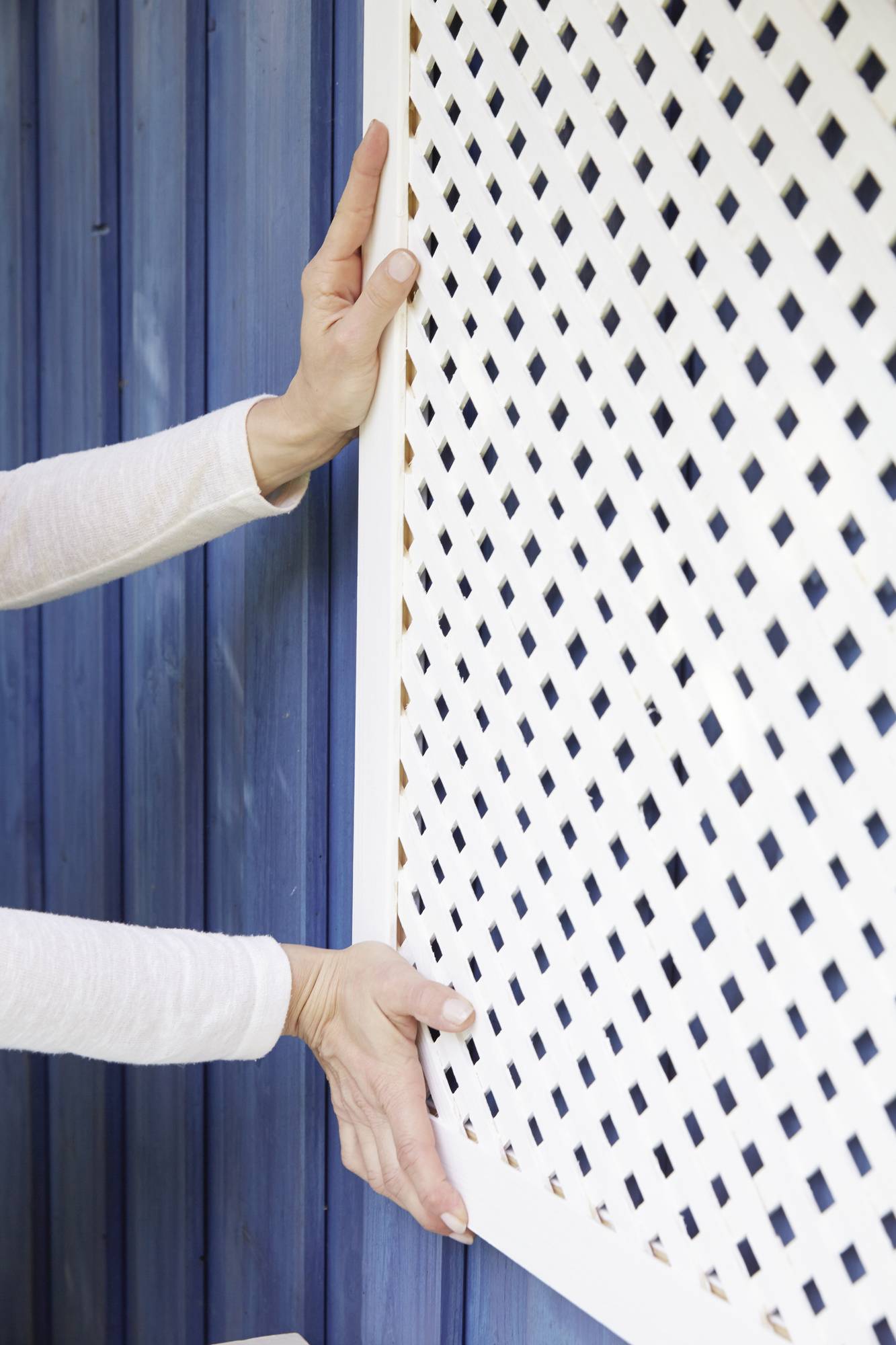 Eine Person montiert ein weißes Gitter vor einer blauen Holzwand.
