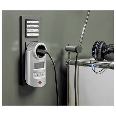 Kopfhörer, die neben einer an der Wand montierten Steckdosenleiste mit Zeitschaltuhr hängen, mit eingestecktem Stecker und einem kleinen digitalen Display.