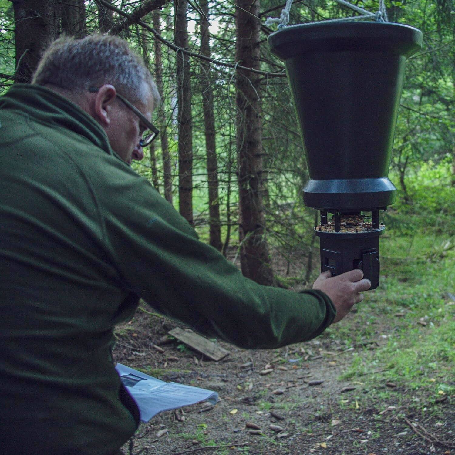 Eine Person justiert eine schwarze Insektenfalle in einer Waldumgebung, mit Bäumen und Unterholz im Hintergrund, was auf eine Forschungsaktivität hindeutet.