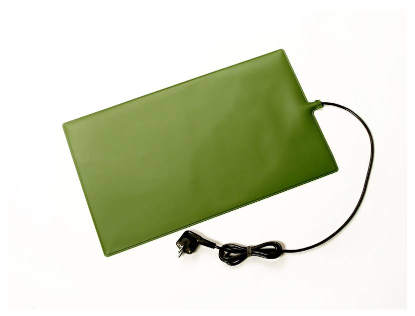 Ein grünes rechteckiges Heizpad mit angeschlossenem schwarzem Stromkabel und Stecker, konzipiert zur Verwendung auf Pflanzentablets oder in kleinen Tiergehegen.