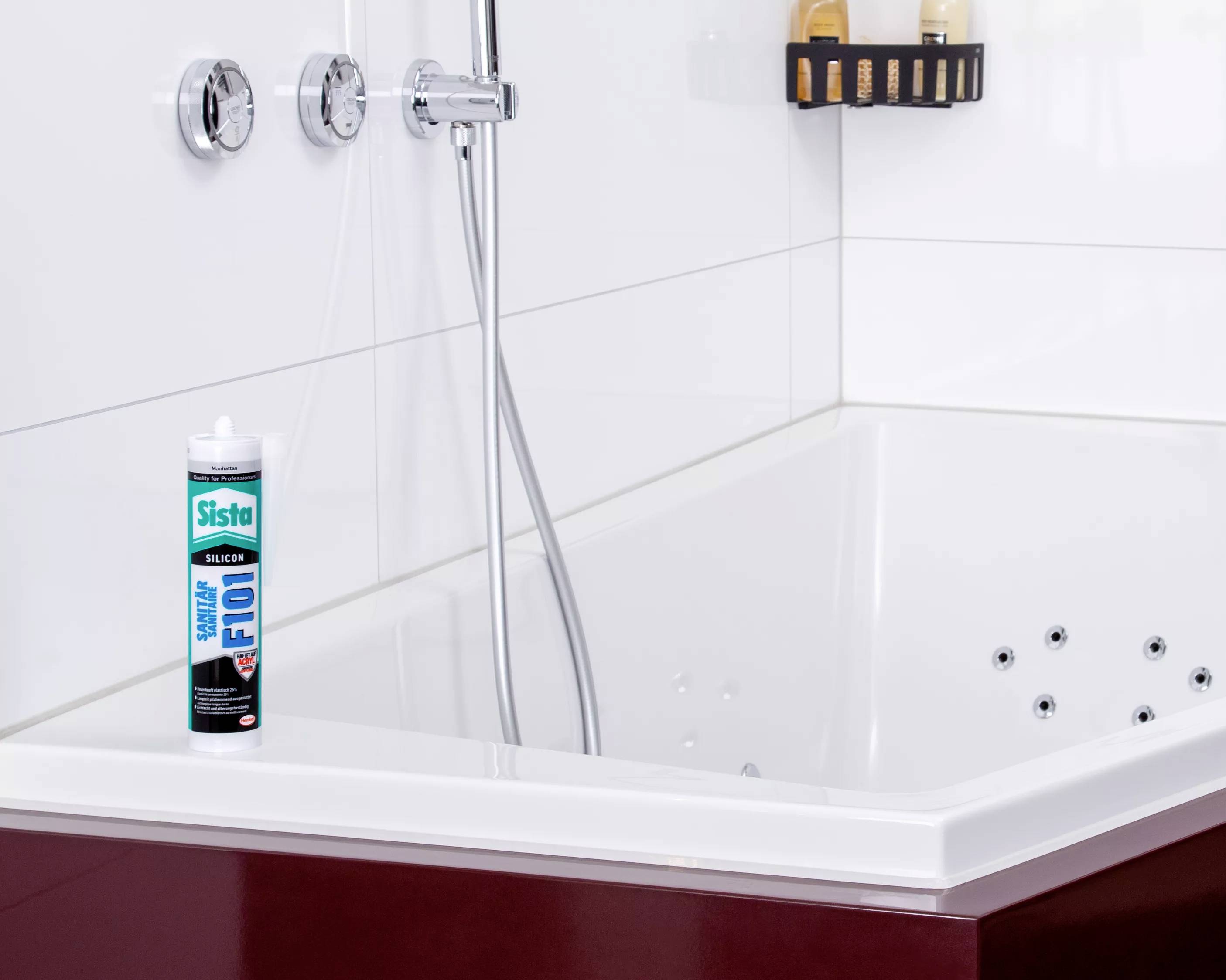 Eine Tube Silikon-Dichtstoff steht am Rand einer weißen Badewanne mit Armaturen an der Wand.