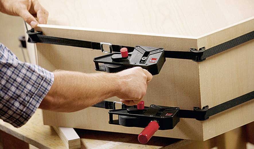 Eine Person verwendet Spannbänder, um Holzteile fest zusammenzuhalten.