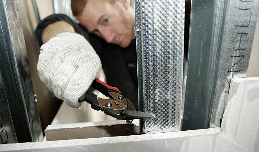 Ein Handwerker schneidet ein Metallprofil mit einem Seitenschneider. Er trägt einen weißen Handschuh und konzentriert sich auf die Arbeit.