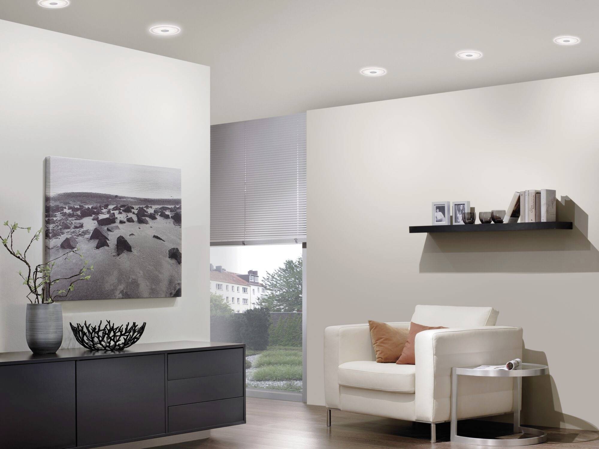 Ein modern eingerichtetes Wohnzimmer mit einem weißen Sessel, einem schwarzen Regal mit Büchern und einer Fotografie an der Wand.