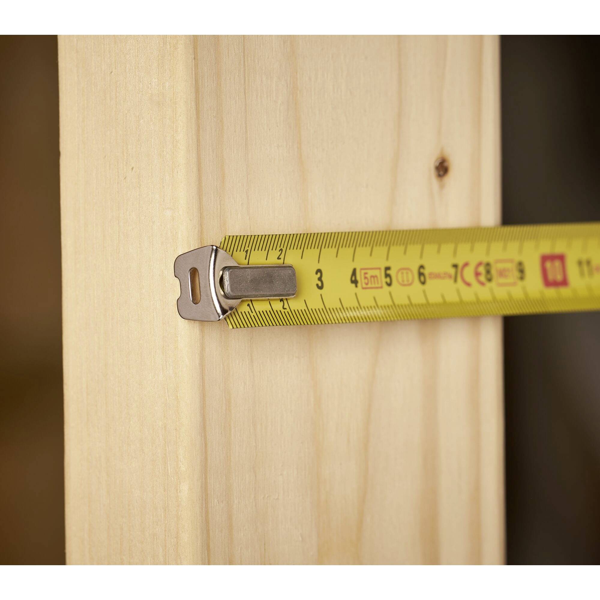 Eine gelbe Maßband zeigt 3 Zentimeter auf einem hellen Holzbrett, das senkrecht steht.