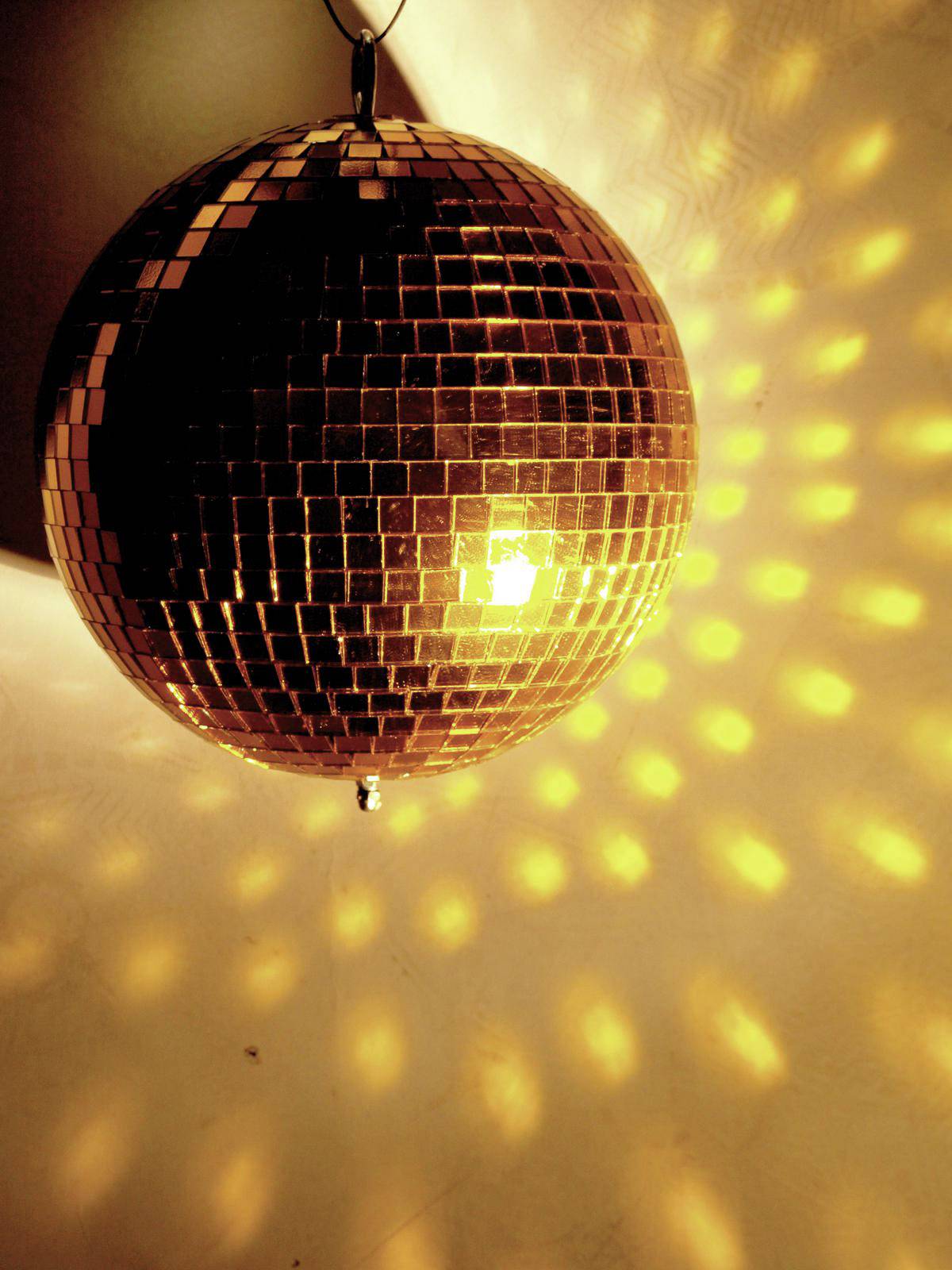 Eine Disco-Kugel reflektiert warmen, gelben Lichteffekt auf die Wand, schafft eine stimmungsvolle, retroartige Atmosphäre.