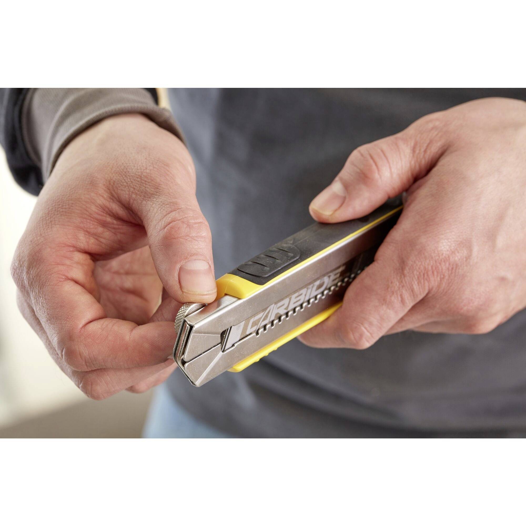 Eine Person hält ein silbernes Teppichmesser mit gelben Akzenten und öffnet es vorsichtig mit den Fingern.