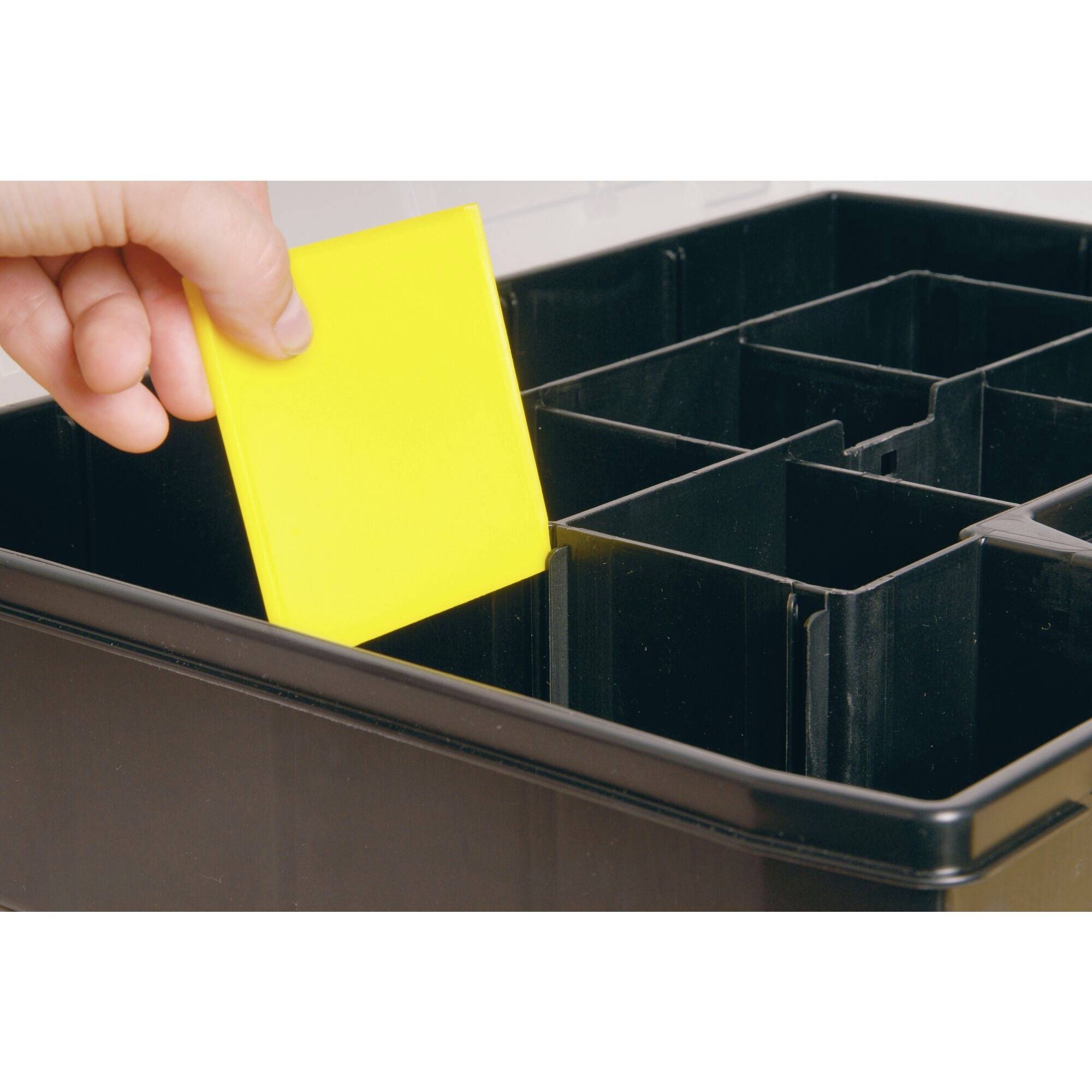 Eine Hand legt eine gelbe Trennwand in eine schwarze Sortimentsbox mit mehreren Fächern.