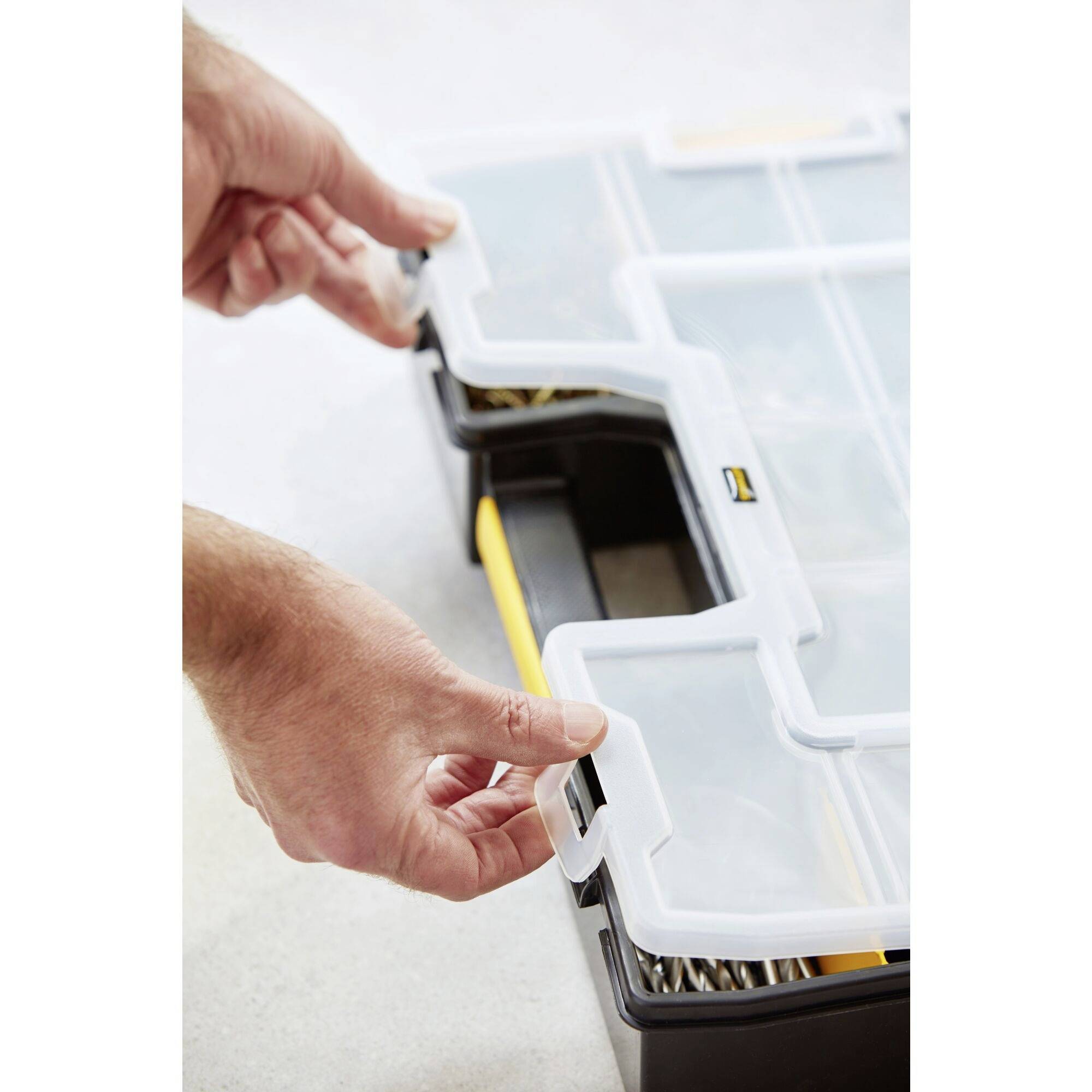 Eine Hand öffnet einen transparenten Kunststoff-Deckel einer Werkzeugbox mit mehreren Fächern auf einer Arbeitsfläche.