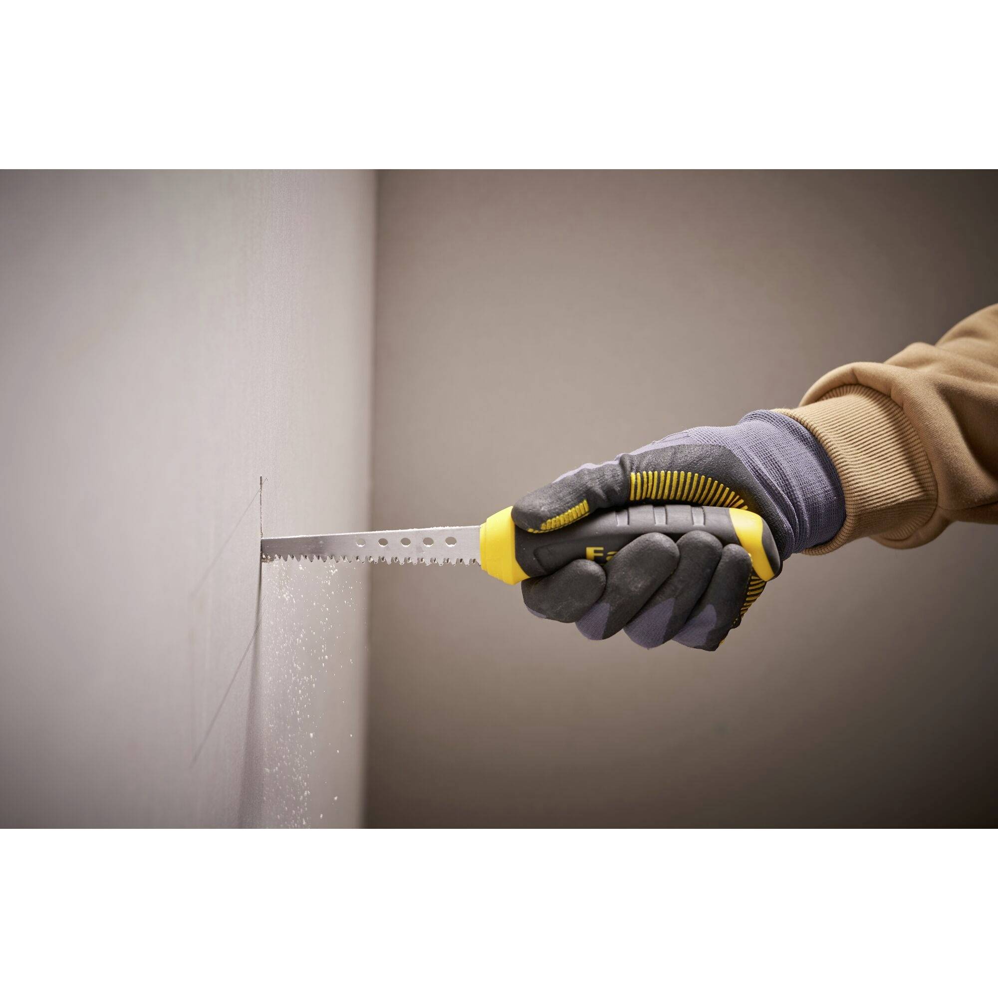 Eine Person schneidet mit einer gelben Handsäge ein Loch in eine weiße Trockenbauwand, trägt dabei Arbeitshandschuhe.